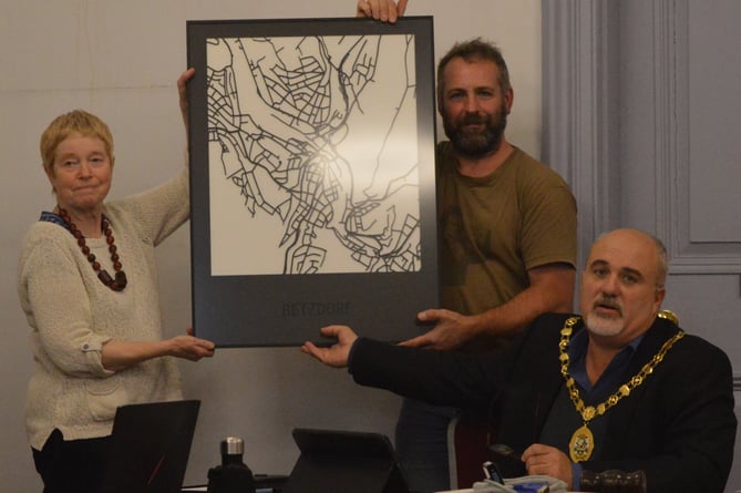 A photo of Cllr Jane Roberts BEM, Cllr John Winder, and Mayor Cllr Ed O’Driscoll with a minimalist painting of Ross-on-Wye.