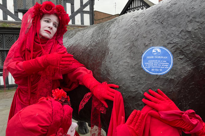 Marches XR next to a parody blue plaque which reads: "Jesse Norman abstained on a vote requiring water companies to dump less raw sewage into our waterways and seas, October 20, 2021".