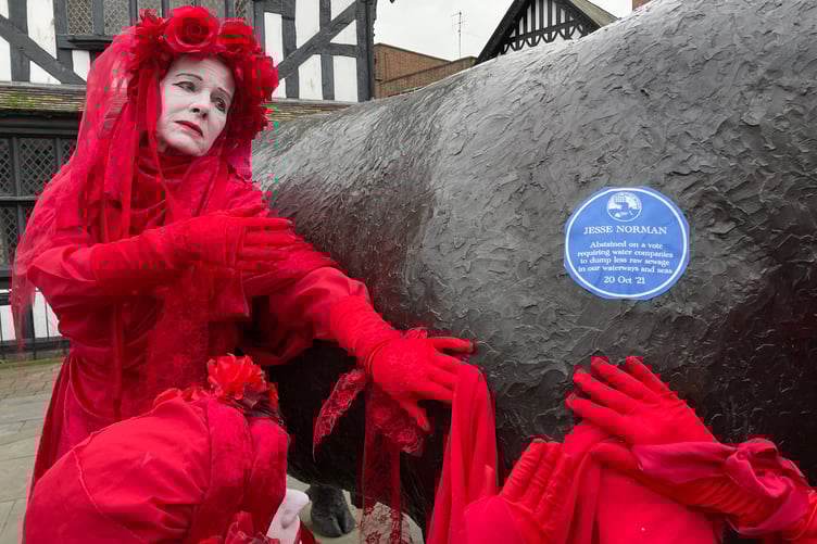 Marches XR next to a parody blue plaque which reads: "Jesse Norman abstained on a vote requiring water companies to dump less raw sewage into our waterways and seas, October 20, 2021".